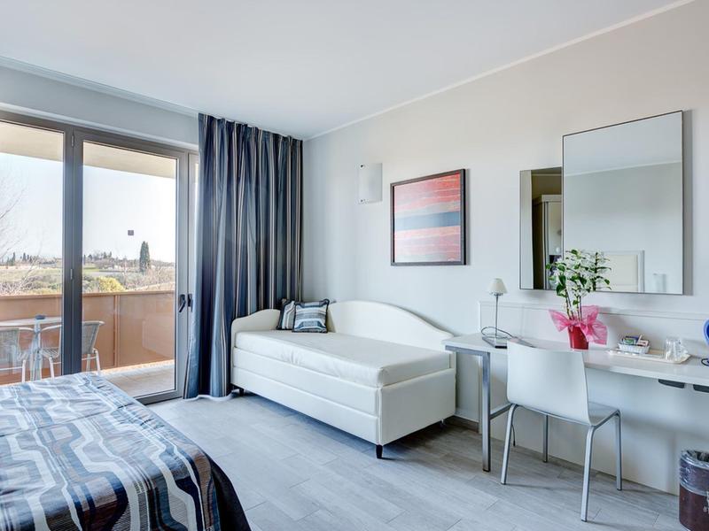 Camera d'hotel moderna con letto, divano, scrivania e balcone con vista.