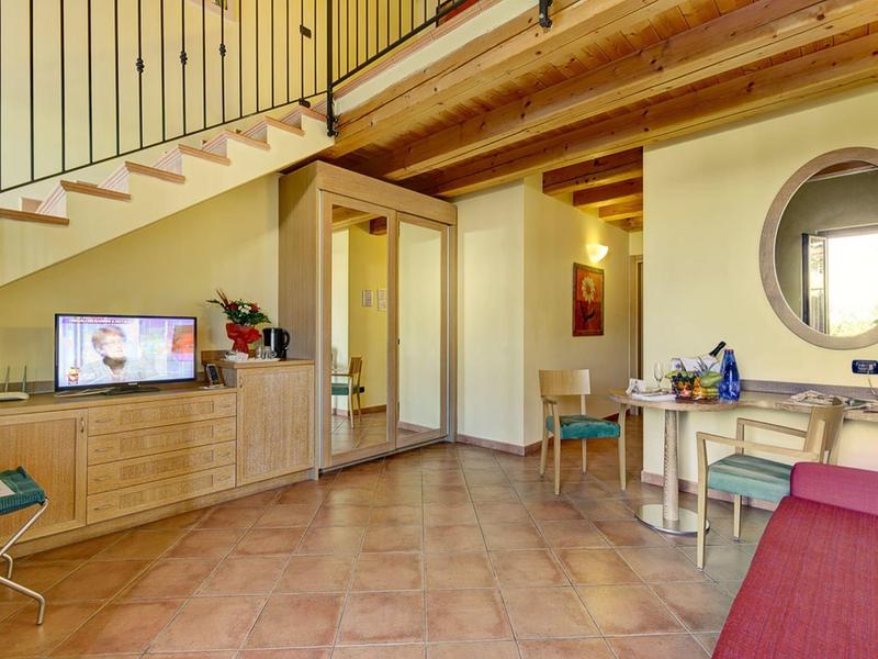 Camera d'hotel luminosa con pavimento piastrellato, mobili in legno e uno specchio rotondo a parete.