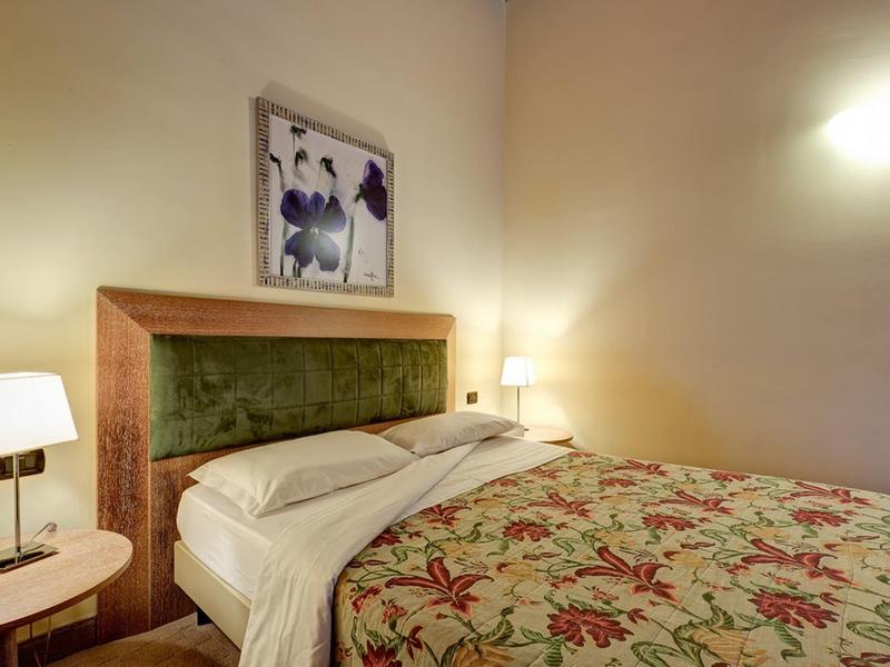 Camera d'hotel accogliente con letto matrimoniale, testiera verde e lampade da tavolo