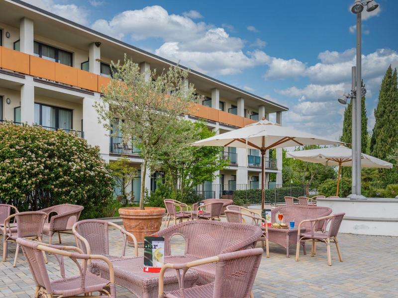 Terrazza con sedie e tavoli rosa davanti a un hotel in una giornata di sole.