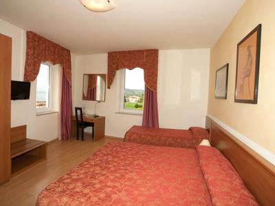 Chambre d'hôtel avec deux lits, un bureau et deux fenêtres avec des rideaux rouges.