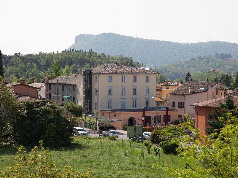 Petit village avec un bâtiment à plusieurs étages devant des collines boisées sous un ciel clair.