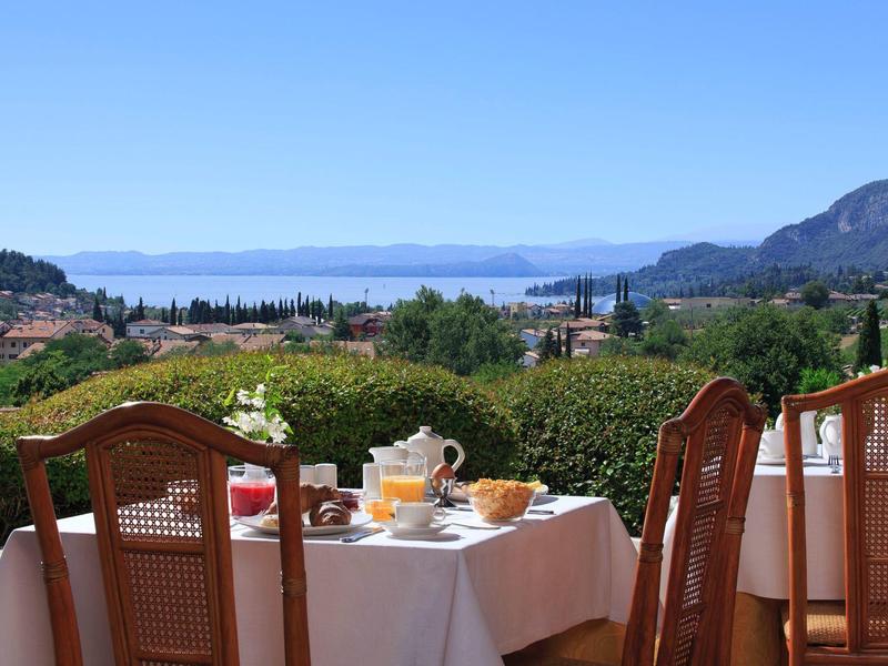 Terrasse mit gedecktem Tisch, Getränke, Ausblick auf Berge, Meer und blaue Himmel.