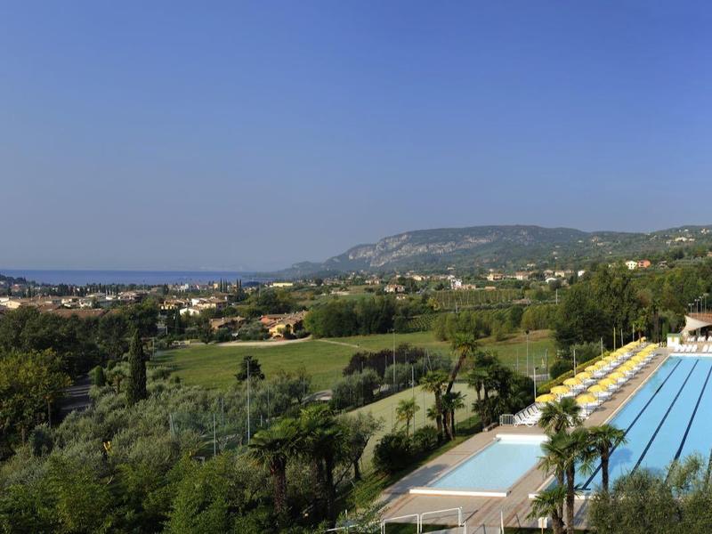 Weite Landschaft mit grünen Hügeln, blauer Himmel und einem großen Pool mit Sonnenschirmen.