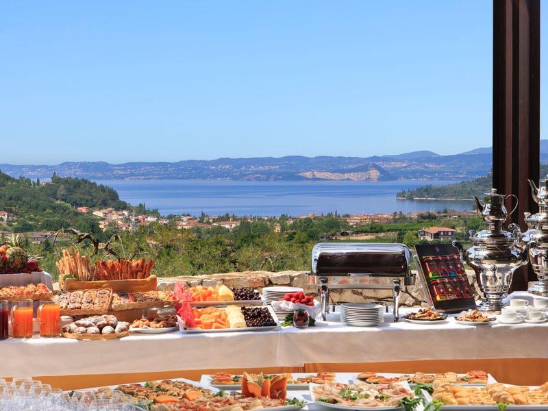 Buffet mit Snacks und Getränken vor Berg- und Seelandschaft unter blauem Himmel.