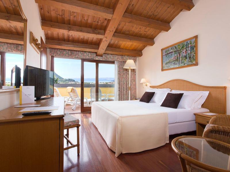 Helles Schlafzimmer mit Holzbalkendecke, großem Bett, TV, Schreibtisch und Balkon mit Bergblick.