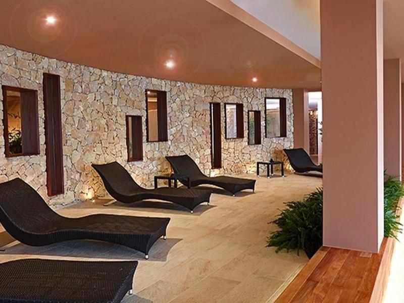 Moderner, heller Raum mit Steinwänden, schwarzen Liegen und Holzboden, sanfte Beleuchtung.