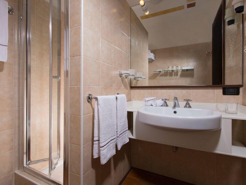 Kleines Badezimmer mit Dusche, weißem Waschbecken, großen Fliesen und Spiegelwand.