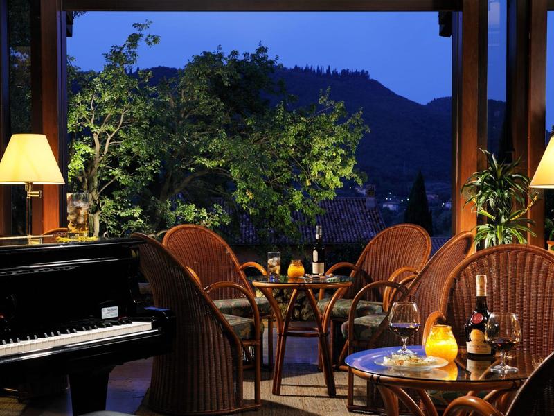 Gemütliche Terrasse mit Rattanmöbeln, Kerzenlicht und Klavier, umgeben von Pflanzen und Bergblick bei Dämmerung.