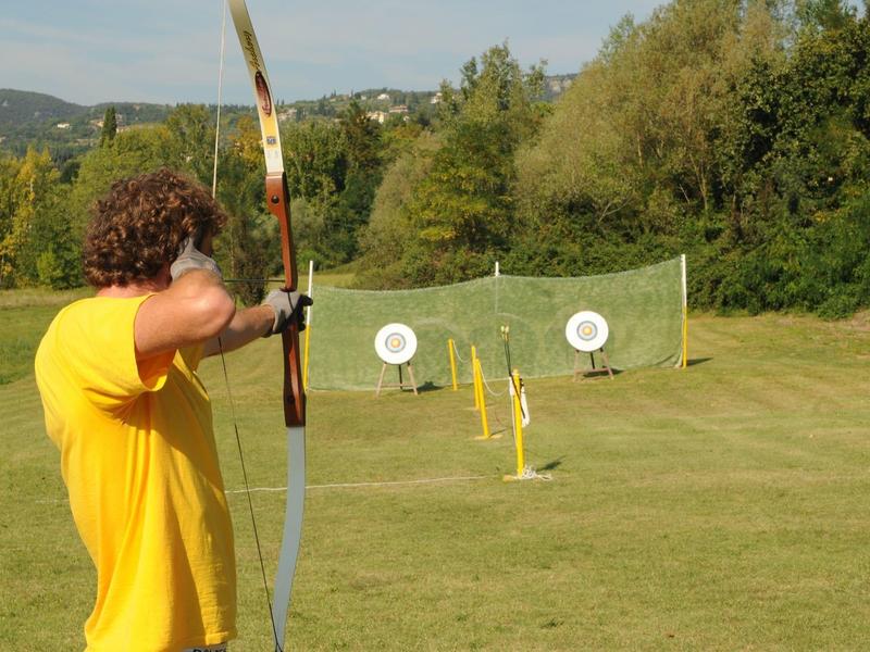 Ein Mann mit gelbem T-Shirt schießt mit einem Bogen auf drei Zielscheiben im Freien.