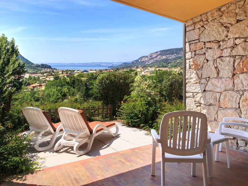 Terrasse mit weißen Stühlen und Liegestühlen, Blick auf grüne Landschaft und blauen Himmel.