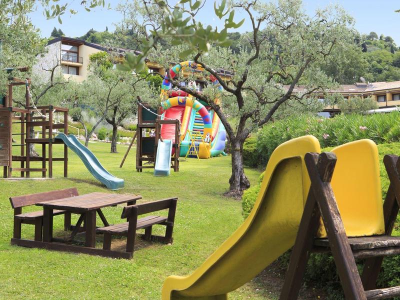 Grüner Spielplatz mit Rutsche, Klettergerüst, Picknicktisch und buntem Hüpfburg-Hintergrund.