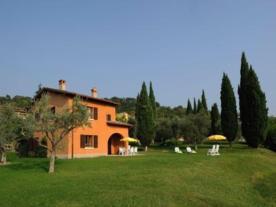 Una casa naranja con terraza en un gran césped verde y cipreses al fondo.