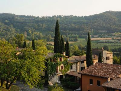 Vista de un pueblo con cipreses y montañas al fondo en un día soleado.