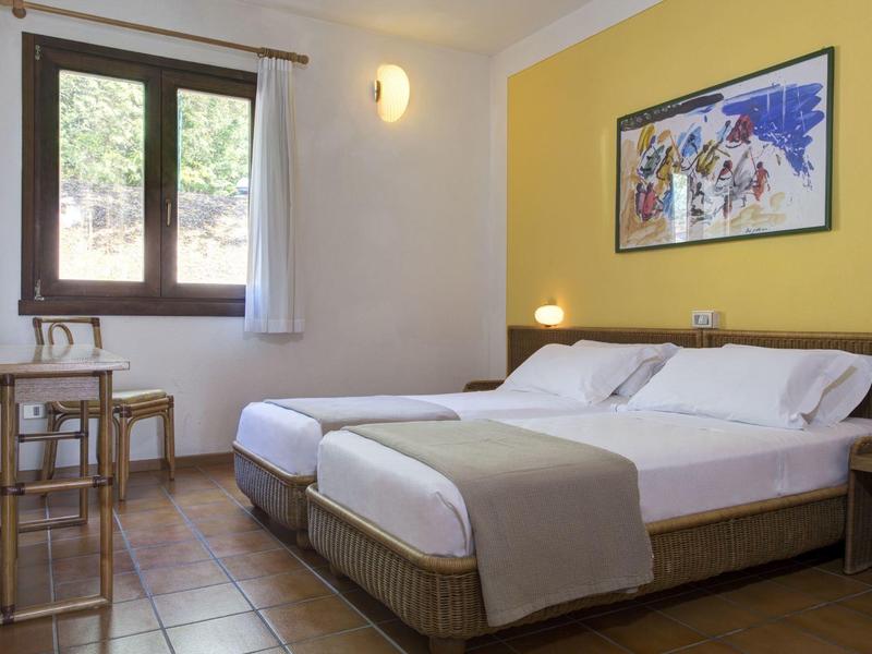 Helles Schlafzimmer mit zwei Einzelbetten, gelber Wand, Holzfenster und einfachem Mobiliar.