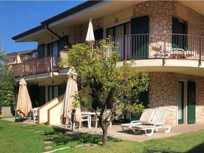 Modernes zweistöckiges Haus mit Natursteinfassade, grünem Rasen, Sonnenschirmen und Liegestühlen.