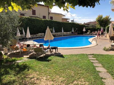 Okrągły basen na zewnątrz w zadbanym ogrodzie z leżakami i parasolami