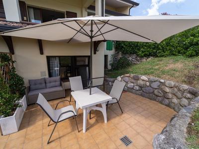 Terrasse mit Tisch, vier Stühlen und Sonnenschirm neben einem Haus mit Garten