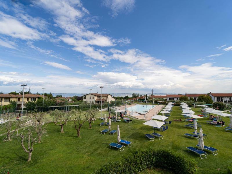 Amplio césped con sombrillas cerradas y tumbonas en un hotel bajo un cielo parcialmente nublado.