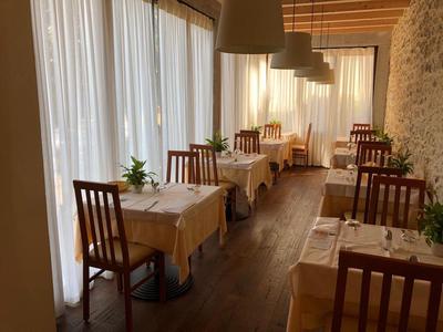 Acogedora zona de comedor con suelos de madera, cortinas blancas y pequeñas mesas con plantas verdes.