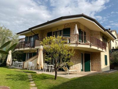 Casa de dos pisos de piedra con balcón y jardín bajo cielo nublado en un entorno vacacional.