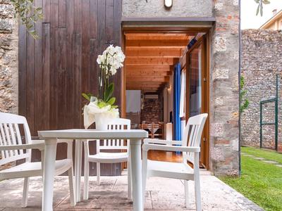 Terraza acogedora con mesa y sillas blancas frente a puerta de madera y muro de piedra