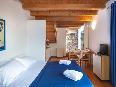 Acogedor dormitorio con ropa de cama azul, techo con vigas de madera y pequeño comedor.