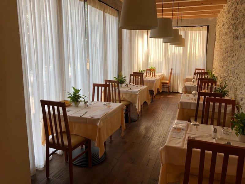 Acogedora zona de comedor con suelos de madera, cortinas blancas y pequeñas mesas con plantas verdes.