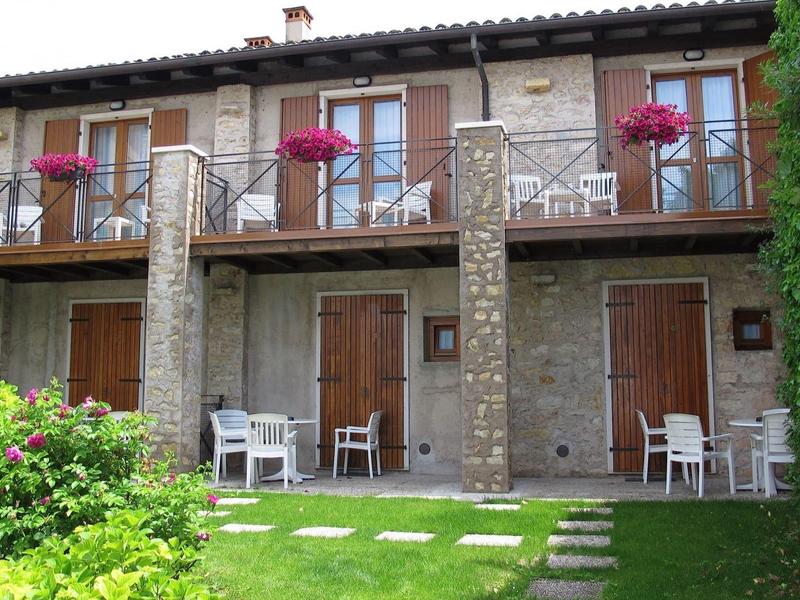 Casa vacacional de piedra con balcón, flores y áreas de jardín con asientos.