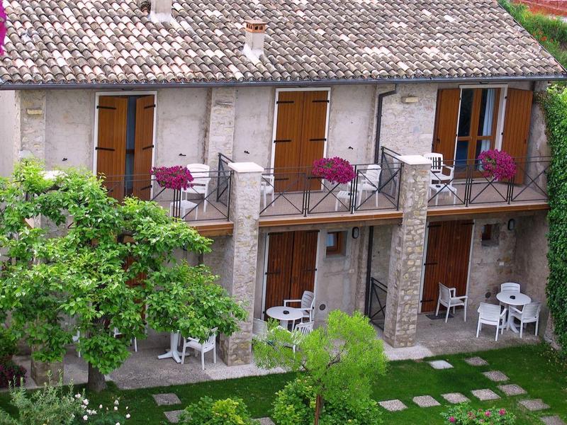 Casa de piedra con balcones y zonas de descanso en el jardín, rodeada de vegetación verde.