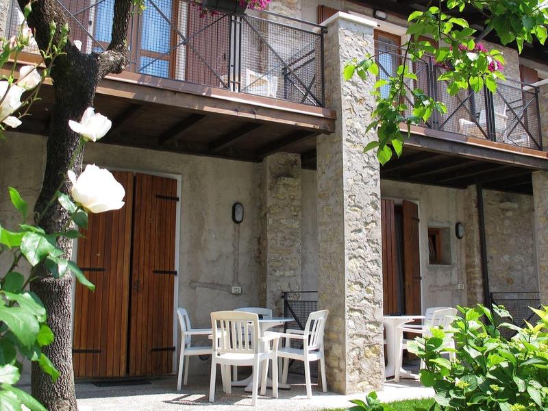 Exterior de piedra con puertas, balcón y mesa blanca con sillas frente a una habitación de hotel.