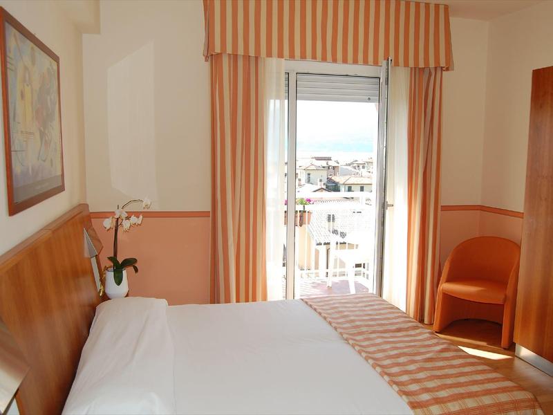 Habitación de hotel luminosa con cama doble, cortinas rayadas naranjas y una silla junto a la ventana.
