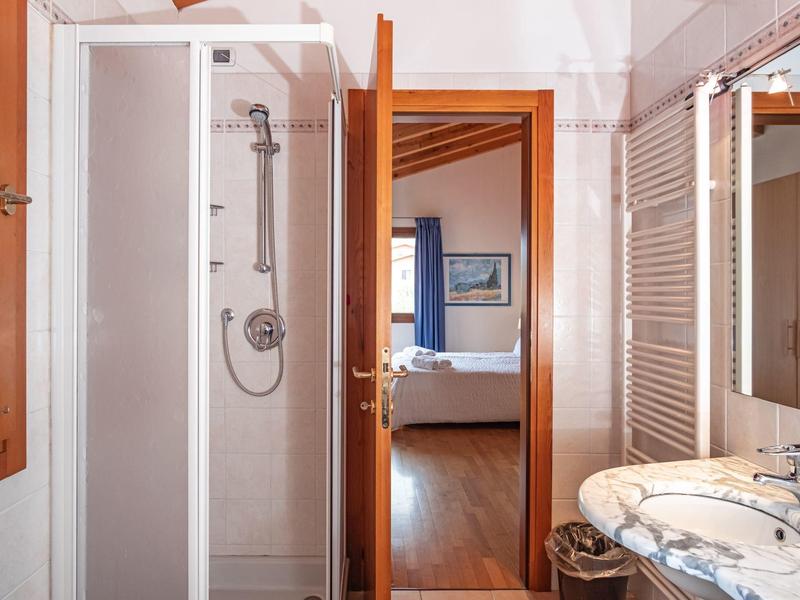 Baño con ducha a nivel, lavabo con encimera de mármol y vista al dormitorio.