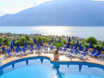 Basen z niebieskimi leżakami i parasolami z widokiem na jezioro i góry.