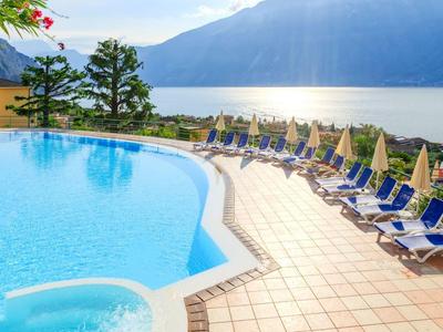 Großer Swimmingpool mit blauen Liegestühlen und Sonnenschirmen neben Berg- und Seeblick.