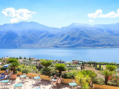 Widok na taras z stolikami i roślinami z widokiem na jezioro i góry w tle.