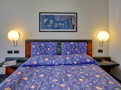 Łóżko podwójne z niebieską pościelą w kwiaty i oświetlonymi lampami ściennymi w pokoju hotelowym.