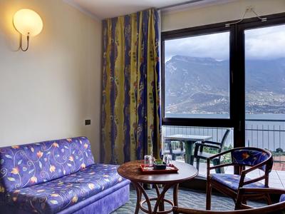 Przytulny kąt pokoju hotelowego z sofą, stołem, krzesłami i widokiem na jezioro i góry.