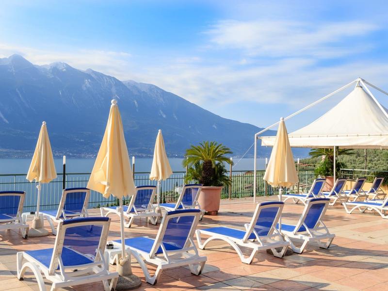 Słoneczny taras z niebieskimi leżakami z widokiem na góry i jezioro pod niebieskim niebem.