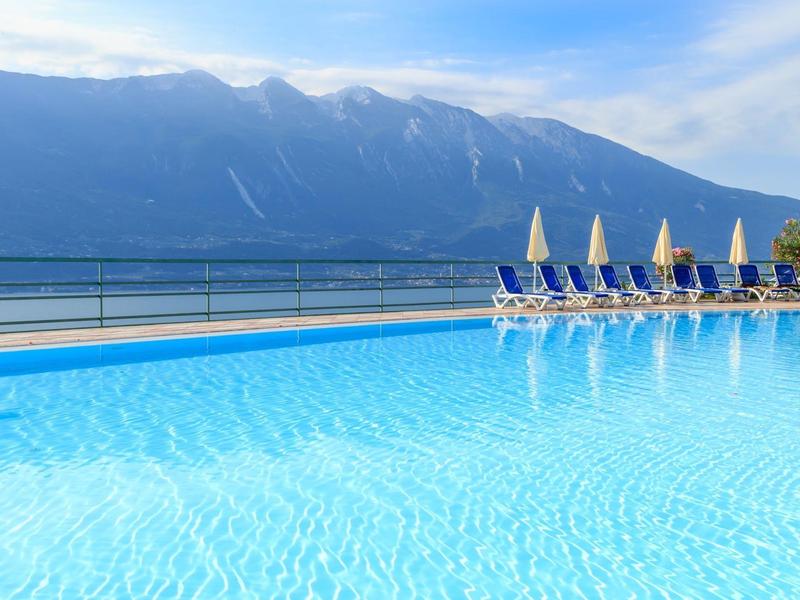 Czysty basen z leżakami i górami w tle w słoneczny dzień.