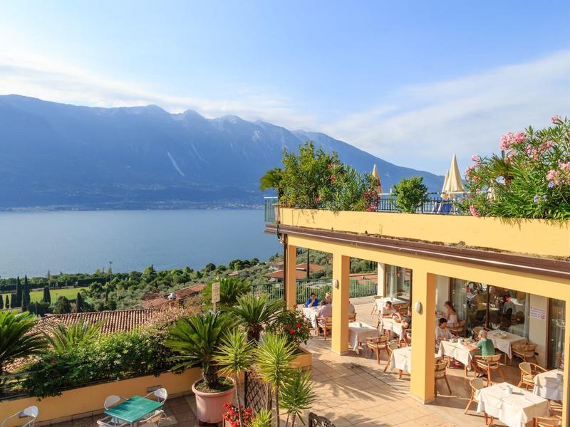 Taras z stolikami, krzesłami i roślinami z widokiem na jezioro i góry pod czystym niebem