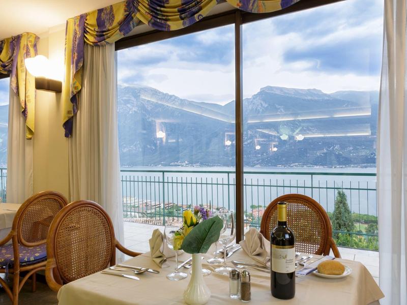 Nakryty stół z winem przed dużym oknem z widokiem na góry i jezioro.
