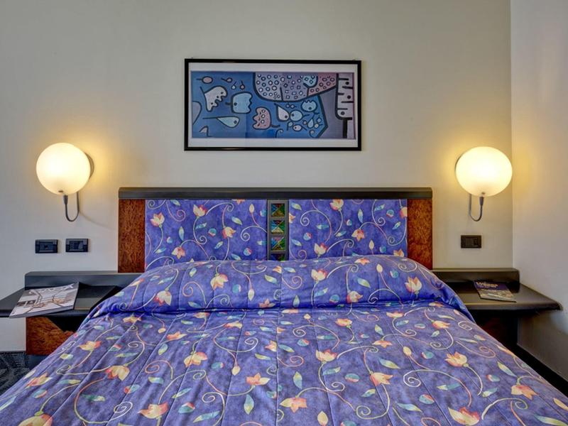 Łóżko podwójne z niebieską pościelą w kwiaty i oświetlonymi lampami ściennymi w pokoju hotelowym.