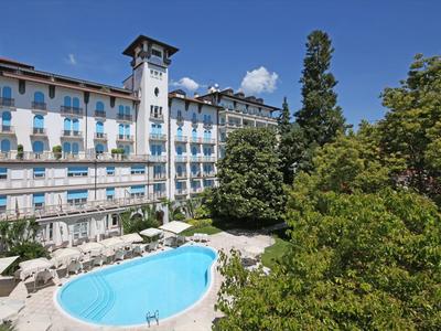Hotel building with outdoor pool, surrounded by trees under clear blue sky.