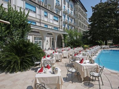 Hotel terrace with set tables beside a pool, surrounded by green plants.