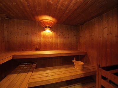 Sauna en bois avec bancs, seau en bois et une lampe murale au plafond.