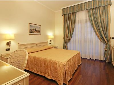 Chambre d'hôtel élégante avec grand lit double, bureau et fenêtre avec rideaux.