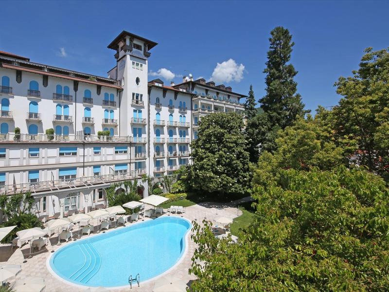 Bâtiment d'hôtel avec grande piscine entourée d'arbres sous un ciel dégagé.