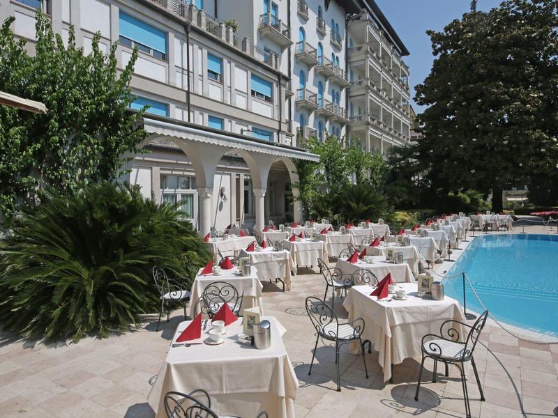 Terrasse extérieure avec tables dressées à côté d'une piscine d'hôtel et beaucoup de verdure.