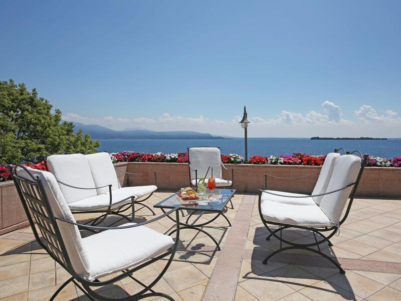 Terrasse avec fauteuils blancs rembourrés et table avec vue sur la mer sous un ciel clair.